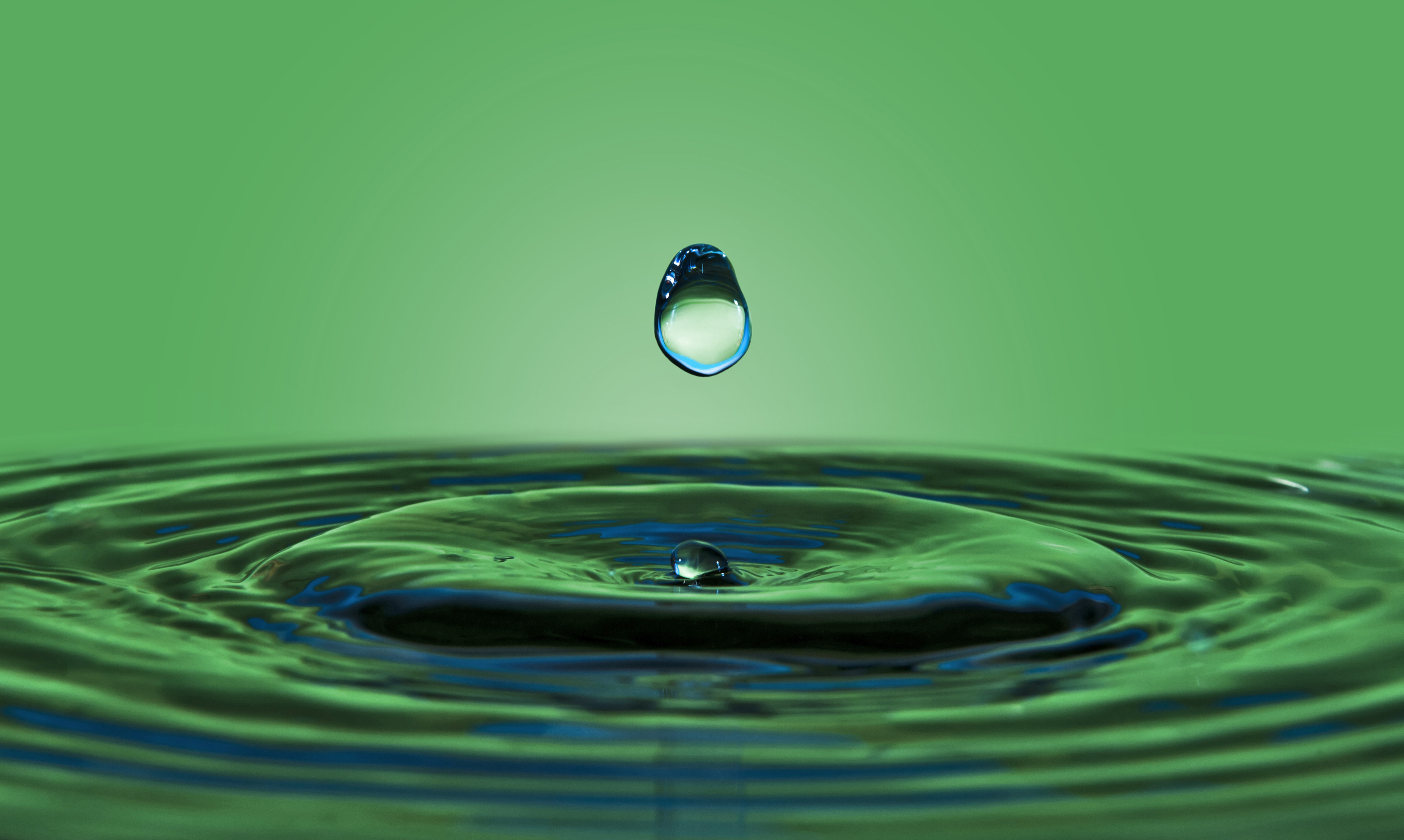 Una goccia d'acqua che cade su una pozza con sfondo verde naturale