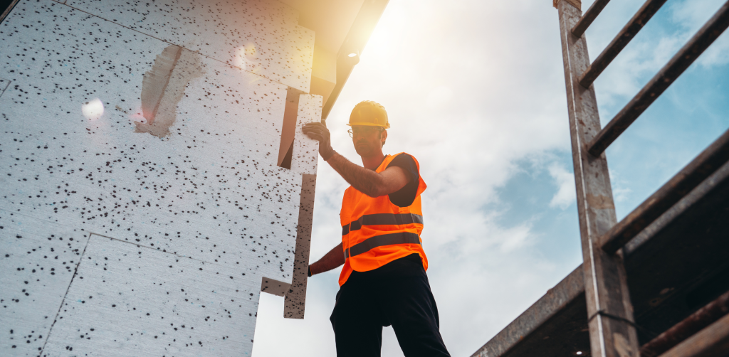 Operaio che installa un isolante termico su un edificio, migliorando l'efficienza energetica e riducendo le dispersioni termiche
