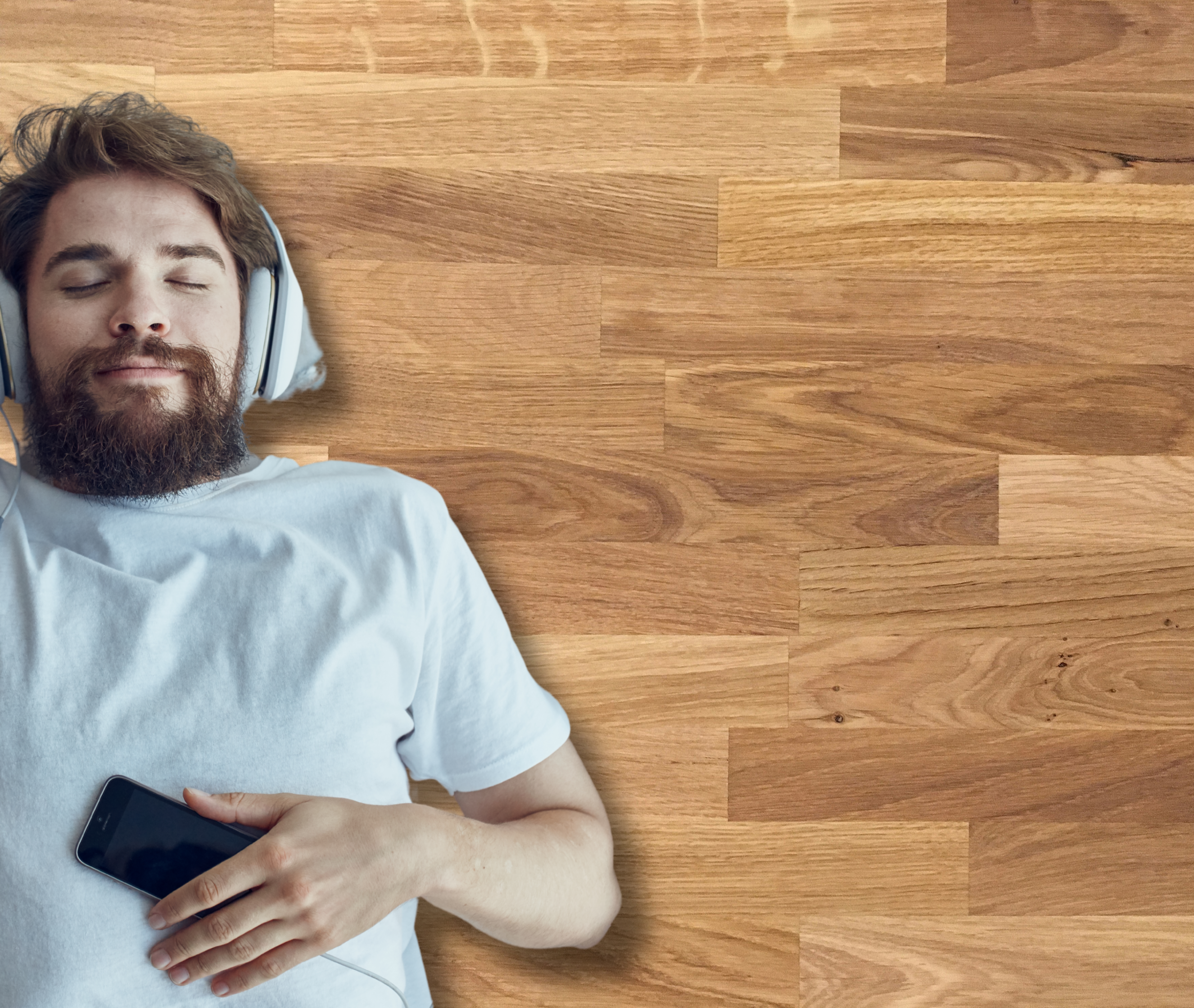 Uomo sdraiato su pavimento in parquet con cuffie, simbolo di comfort abitativo garantito dal raffreddamento a pavimento. Tecnologia invisibile per un relax totale.
