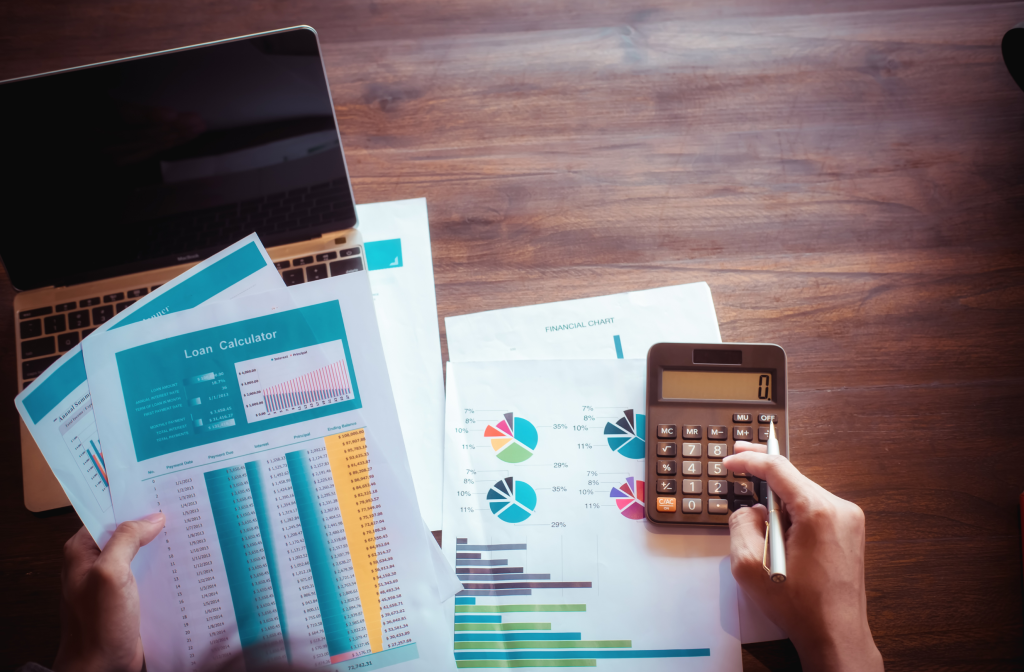 Scena di lavoro su un tavolo con computer, documenti, fogli di calcolo e una calcolatrice, simboleggiando l’analisi dei costi operativi, il confronto tra investimenti iniziali e risparmi a lungo termine per caldaie ibride e pompe di calore."